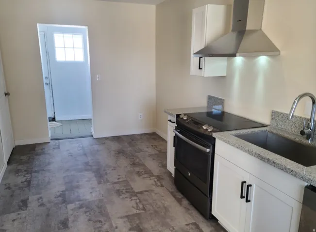Wood-finish flooring, white cabinetry with dark hardware, granite-style countertops, stainless steel sink, and a modern range hood