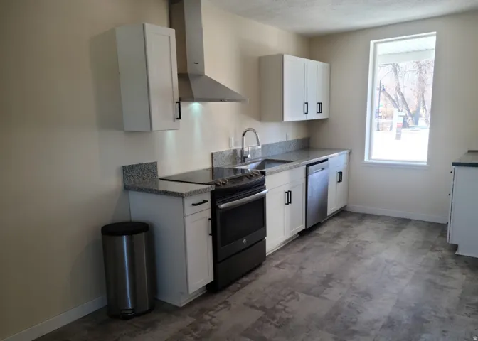 White cabinetry with matte black hardware, stainless steel appliances, speckled stone-finish countertops, and wood-finish flooring