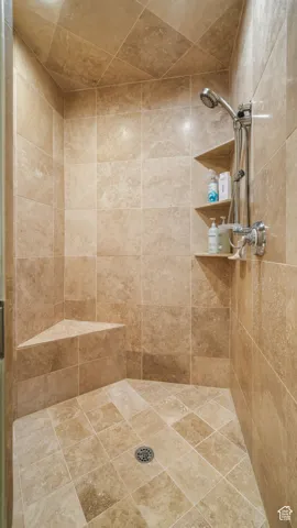 Guest stone walk-in shower with a built-in corner seat, handheld showerhead, and integrated shelving