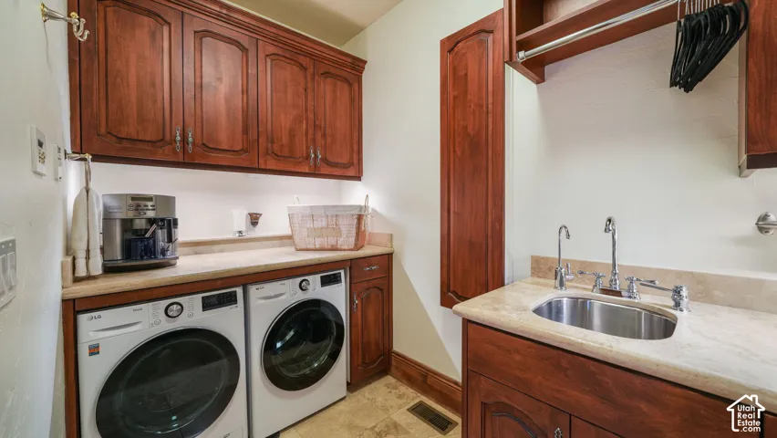 Master ensuite laundry room featuring side-by-side front-load washers and dryers, cherry wood cabinetry with ample storage, quartz countertop with undermount sink, and tile flooring