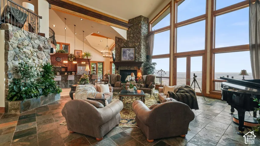 Spacious great room featuring natural stone flooring, a soaring stone fireplace, a grand staircase and large floor-to-ceiling windows