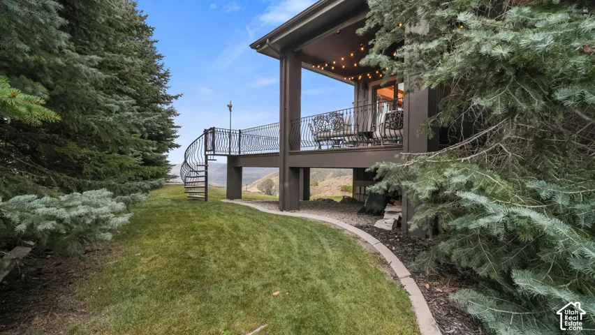 Covered deck with decorative railing, spiral staircase access, and a manicured lawn area