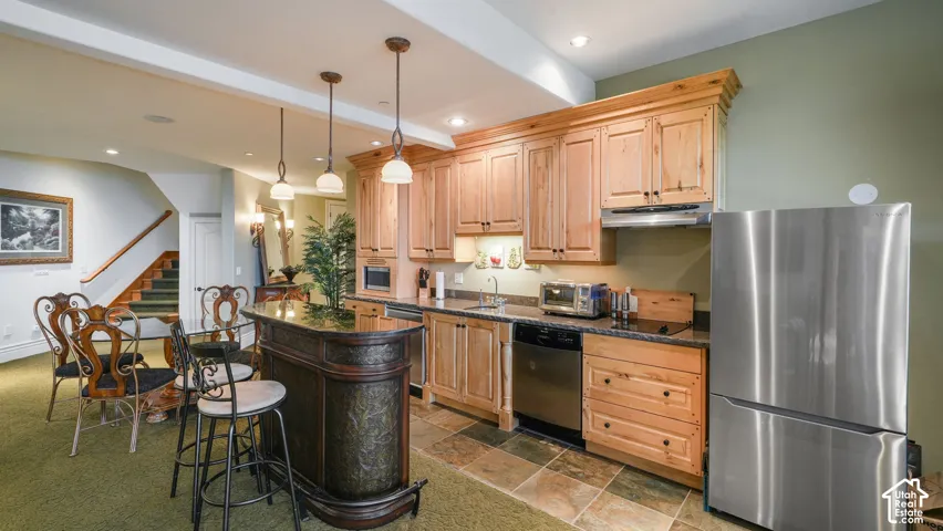 Chef's kitchen featuring natural wood cabinetry, stainless steel appliances, and a stone and carved island with seating