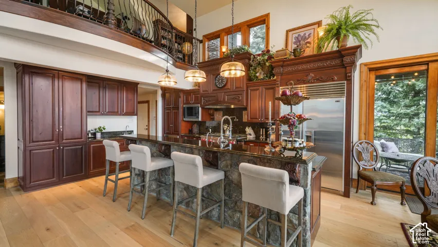 Hardwood flooring, stone-clad kitchen island, dark wood cabinetry, stainless steel appliances, and a balcony