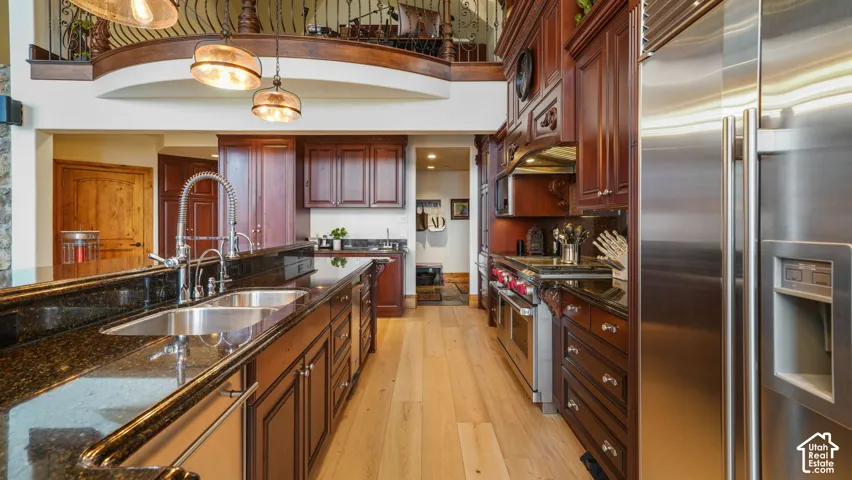 Kitchen featuring dark wood hand-milled cabinetry, with pull out and pull down technology ,granite countertops, stainless steel appliances, wood flooring, and a double basin sink with a gooseneck faucet