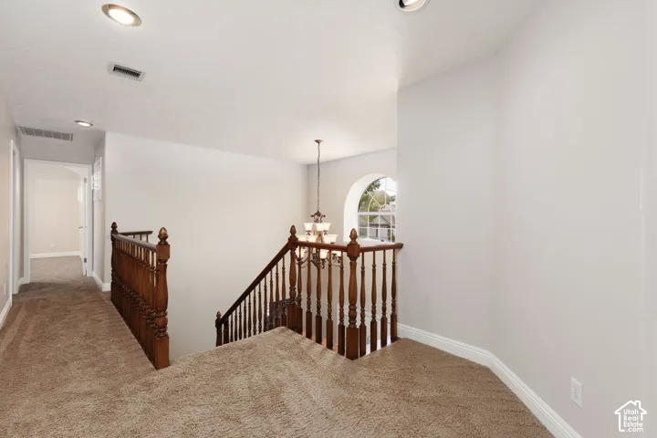 Carpeted hallway and landing, wood newel posts, wood balusters, recessed lighting, and an arched window
