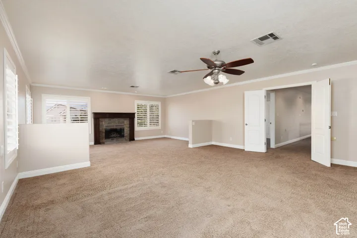 Spacious room featuring a stone fireplace with a wood mantle, multiple windows with plantation shutters, a ceiling fan, and double doors