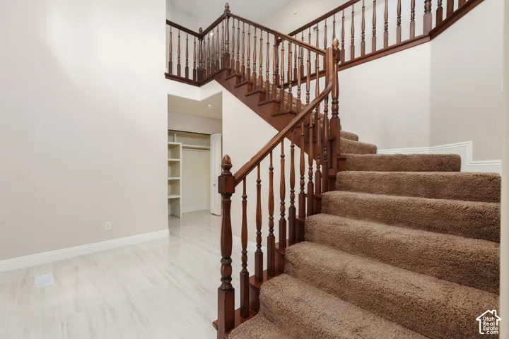 Staircase featuring wood railings and brown carpet treads, complemented by light-toned wall paint and white baseboards