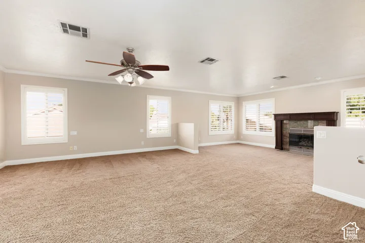 Spacious room featuring neutral carpet, multiple windows with white shutters, a ceiling fan with light fixture, and a fireplace with a wood-finish mantel and tile surround