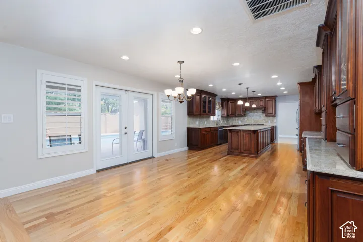 Recessed lighting throughout, wood-finish flooring, French doors with white frames, dark wood cabinetry, and a kitchen island with pendant lighting