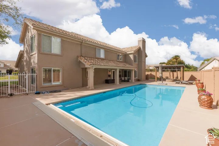 Expansive backyard featuring a rectangular swimming pool, a stucco exterior, a covered patio with columns, and a dedicated patio area with a pergola