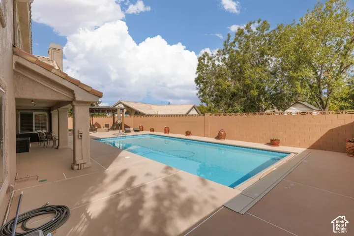 Expansive backyard featuring a rectangular swimming pool, a covered patio, and a privacy wall