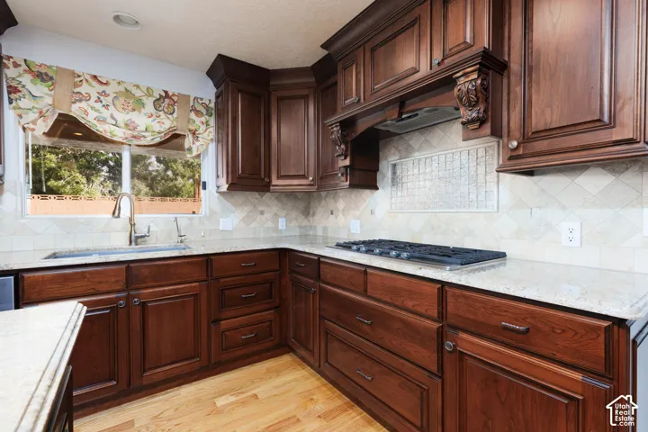 Wood-finish cabinetry with decorative corbels, light-toned countertops, tile backsplash, and a built-in gas cooktop