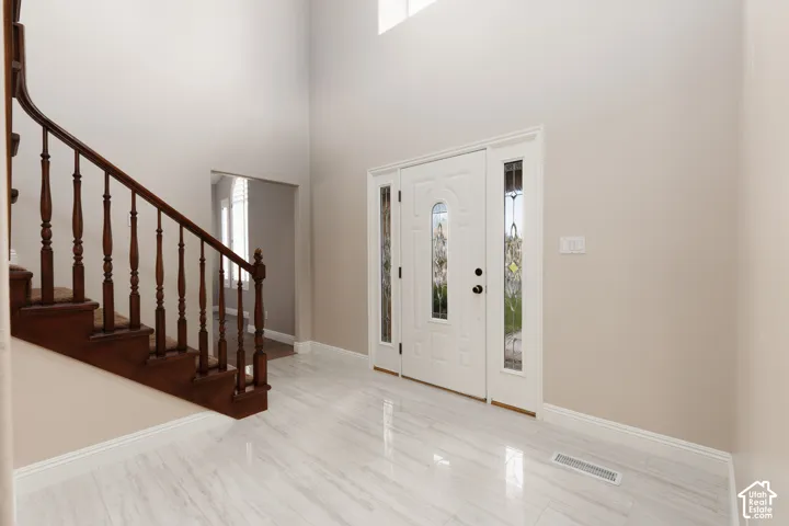Two-story entryway featuring a decorative front door with side lites, a grand staircase with wood newel posts and balusters, and large format tile flooring
