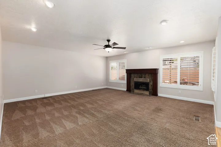 Spacious room featuring neutral carpeting, recessed lighting, and a dark wood mantel over a stone-clad fireplace