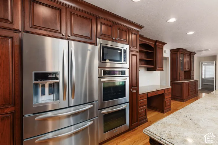Built-in stainless steel appliances, rich wood cabinetry, recessed lighting, wood-finish flooring, and a stone countertop