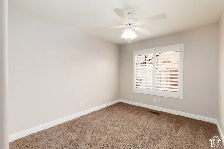 Carpeted room featuring a ceiling fan with integrated lighting, a window with white plantation shutters, and light-colored wall paint