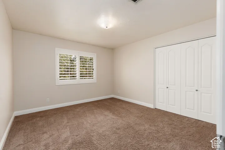Light-colored walls, brown carpet flooring, flush-mount ceiling light fixture, white window shutters, and white bi-fold closet doors