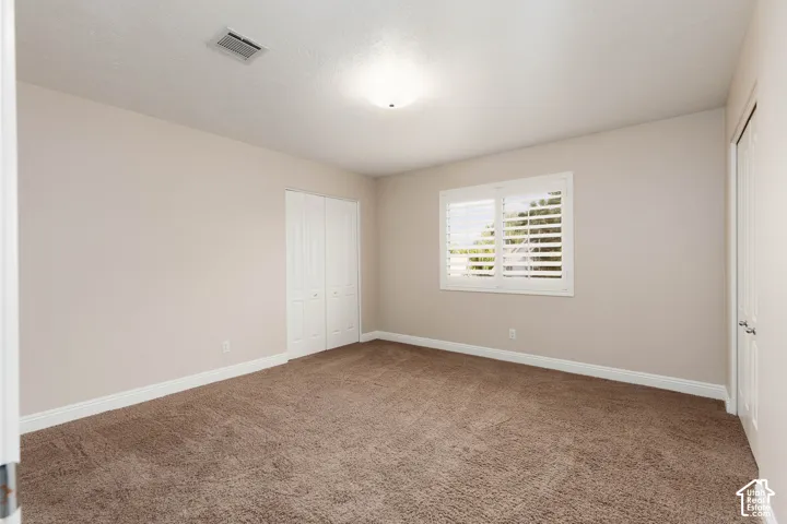 Plush carpet flooring, neutral paint palette, white trim, window with white plantation shutters, and a bi-fold closet door