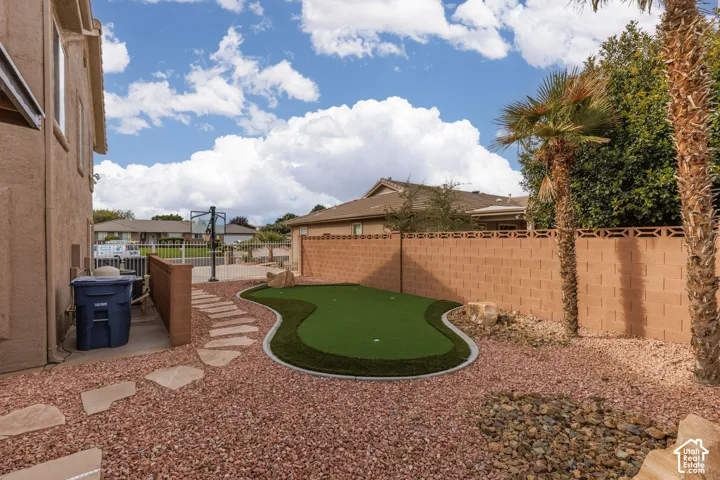 Artificial turf putting green, stone paver pathway, decorative rock landscaping, and mature palm trees