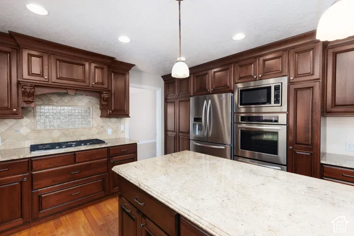 Dark wood cabinetry, stainless steel appliances, light-toned countertops, tile backsplash, and recessed lighting