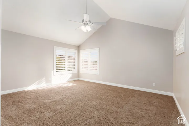 Vaulted ceiling with a ceiling fan, plush carpeting, and multiple windows with plantation shutters