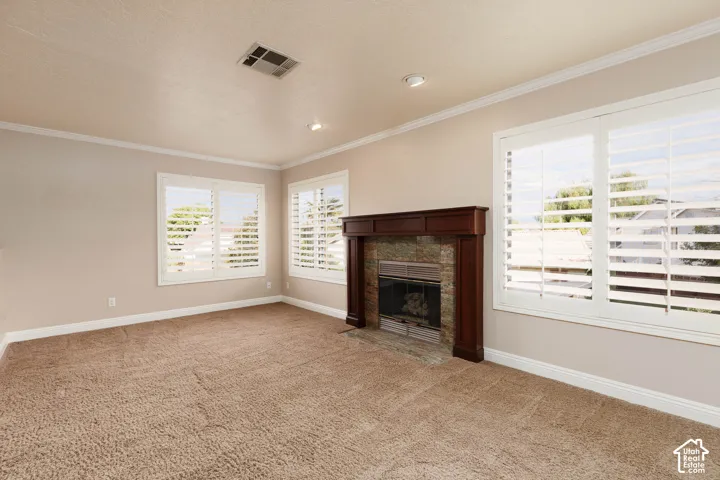 Warmly carpeted room featuring a stone-faced fireplace with a dark wood mantel, white crown molding, recessed lighting, and white window shutters