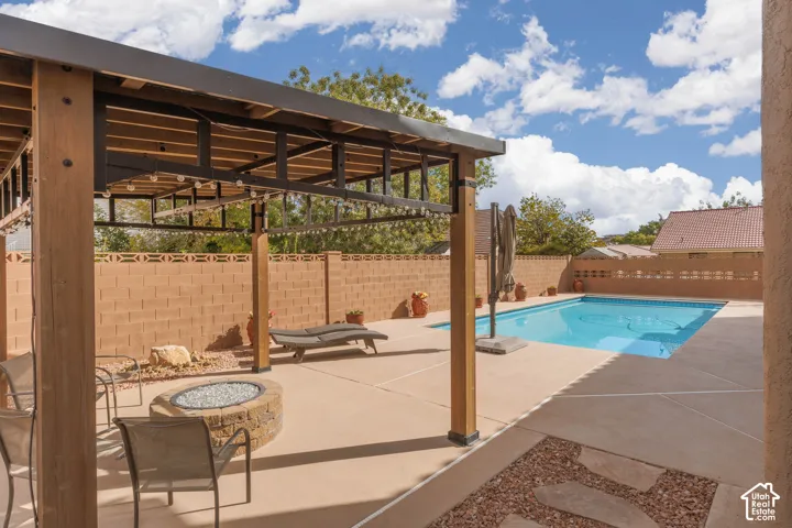 Outdoor living area featuring a wood-beam pergola, built-in fire pit, and a swimming pool with a surrounding concrete patio