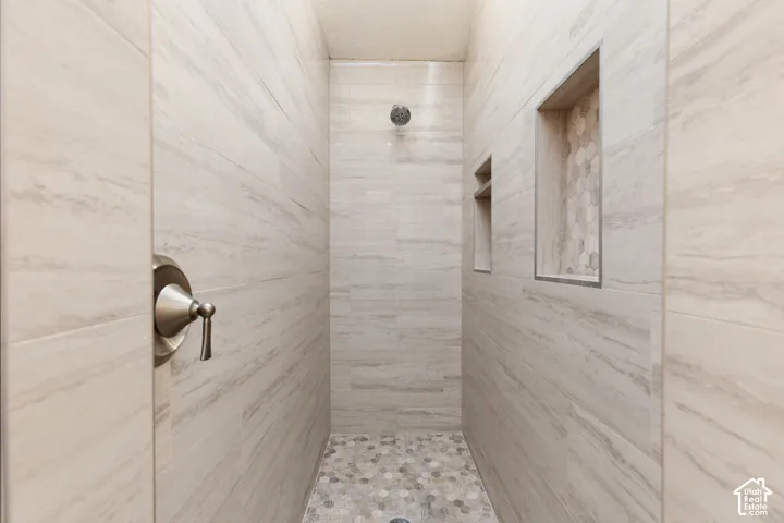 Shower featuring large format tile walls, recessed shelving with hexagonal tile accents, a rain shower head, a brushed nickel shower control, and a pebble tile floor