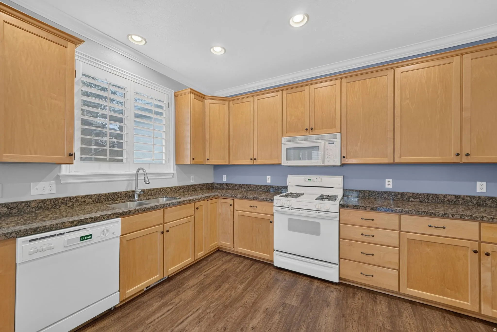 Kitchen featuring wood-finish cabinetry, granite-style countertops, stainless steel sink with a gooseneck faucet, and integrated appliances