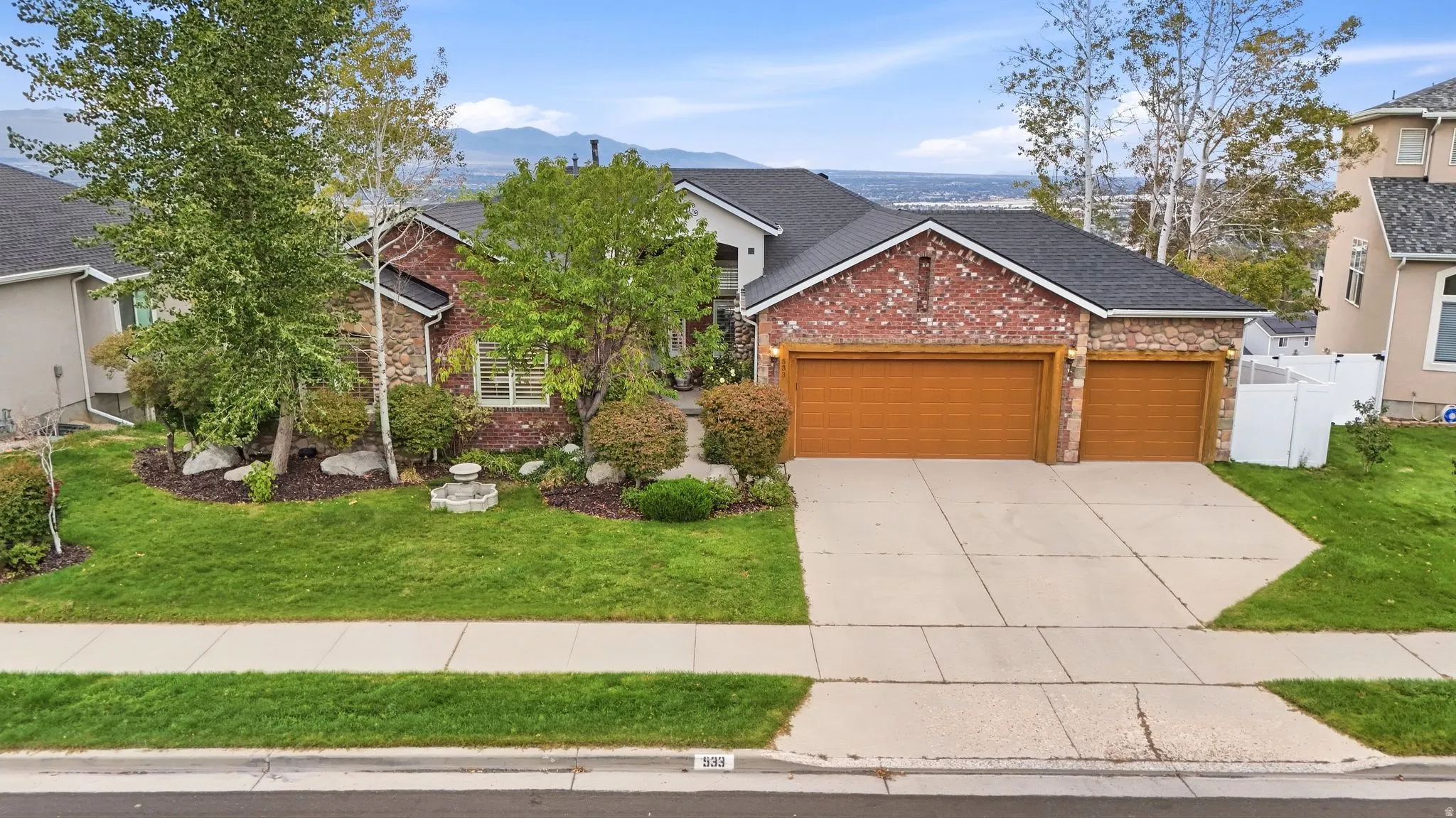 Brick and stone facade with a multi-car garage, mature landscaping, and a manicured lawn