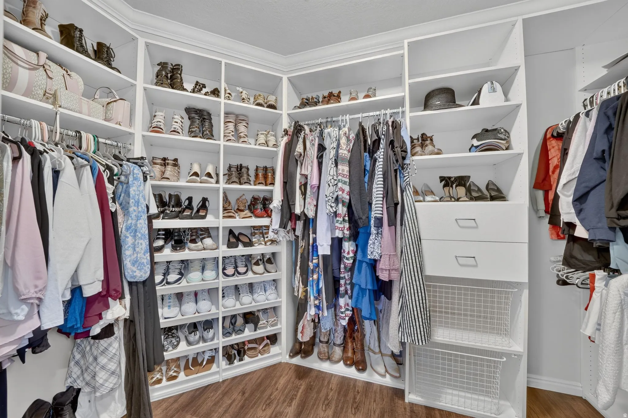 Custom closet system with white shelving, integrated drawers, wire baskets, and wood-finish flooring