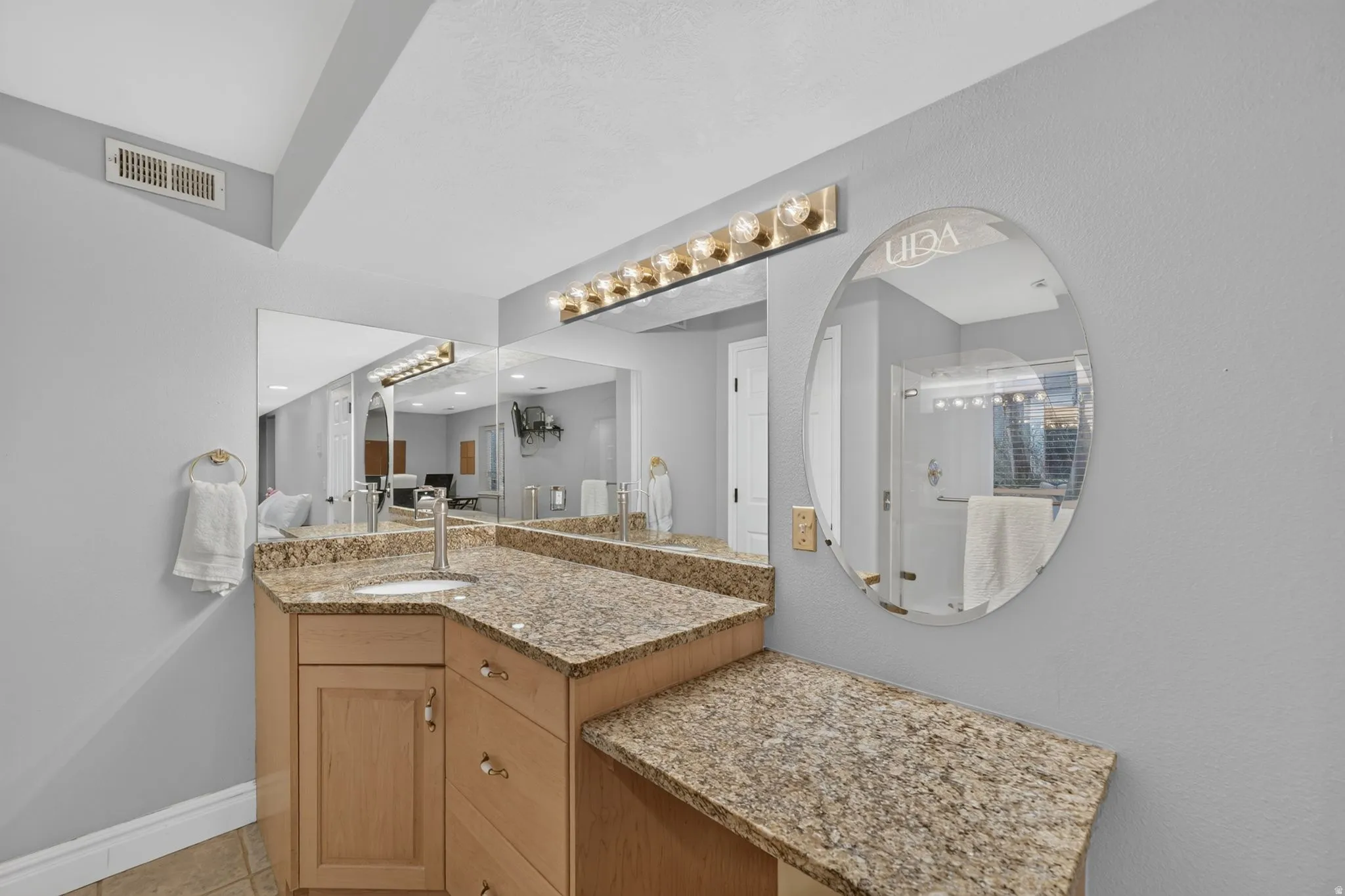 Vanity with an integrated sink and light wood cabinetry, stone-finish countertop, and a vanity light fixture