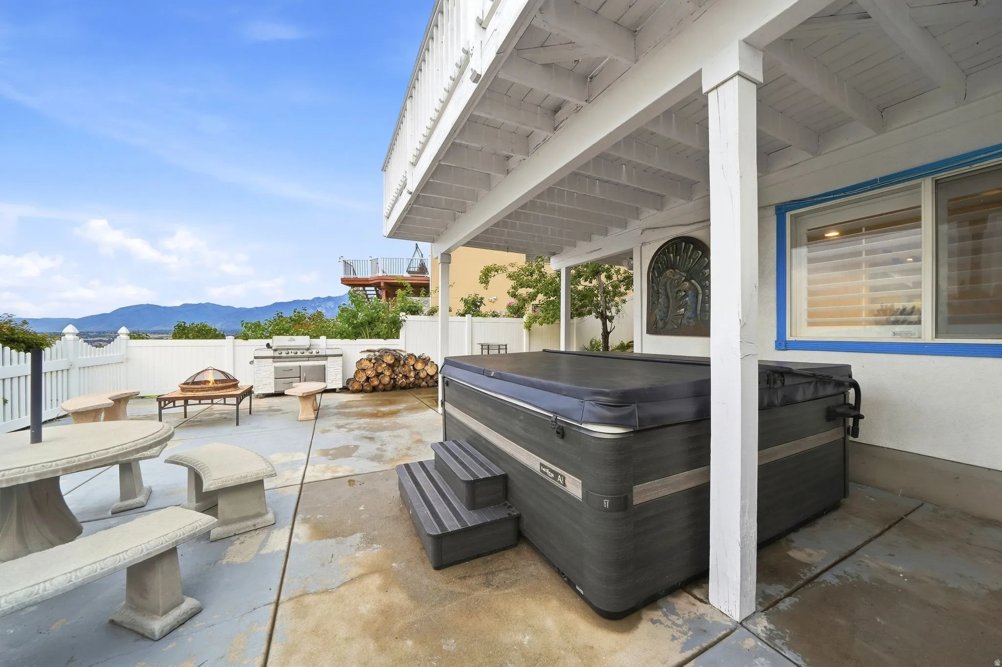 Paved patio with covered area, integrated hot tub, built-in grill, and white picket fencing