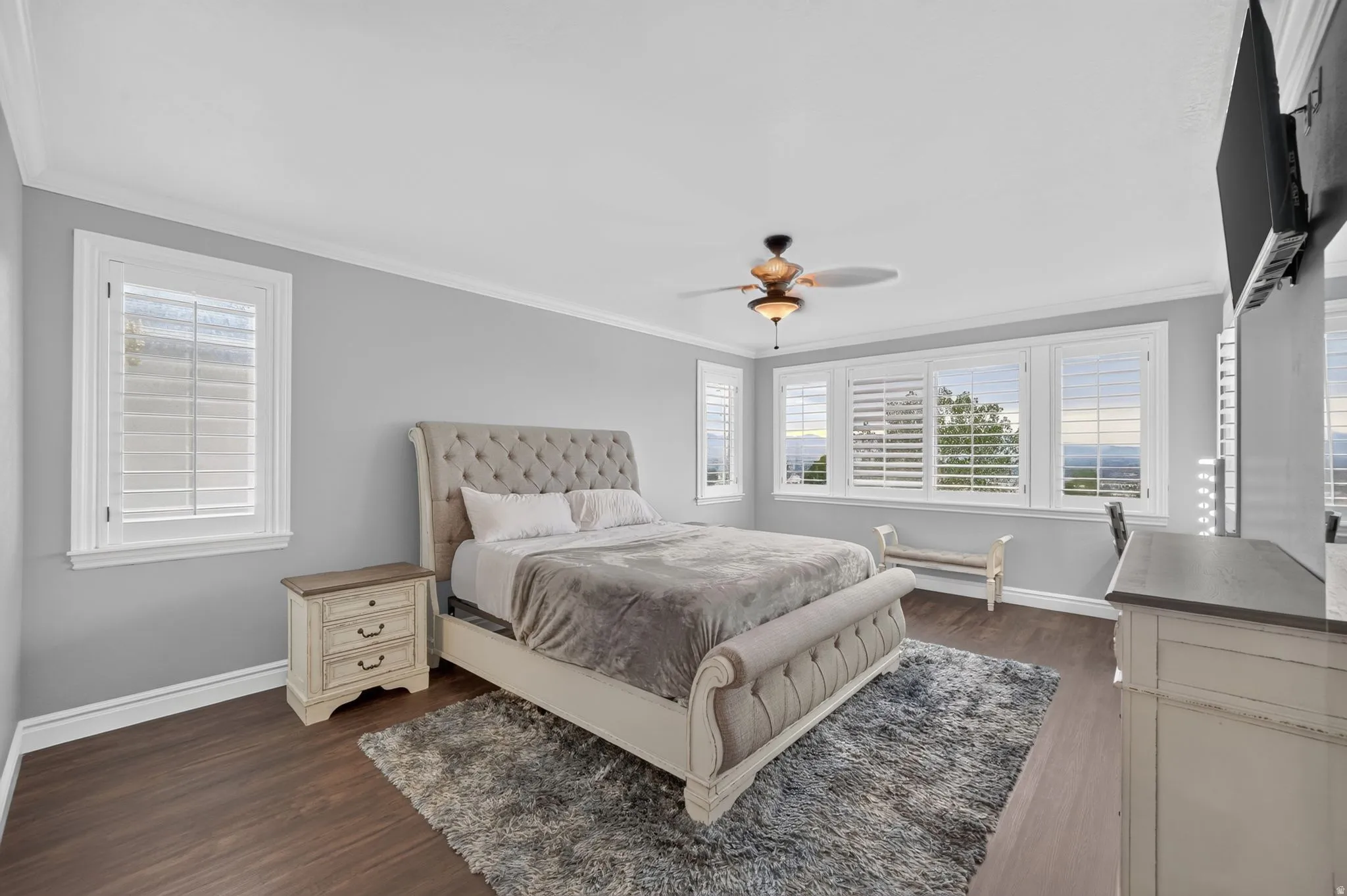 Expansive windows with plantation shutters, crown molding, wood-finish flooring, and a ceiling fan with integrated lighting