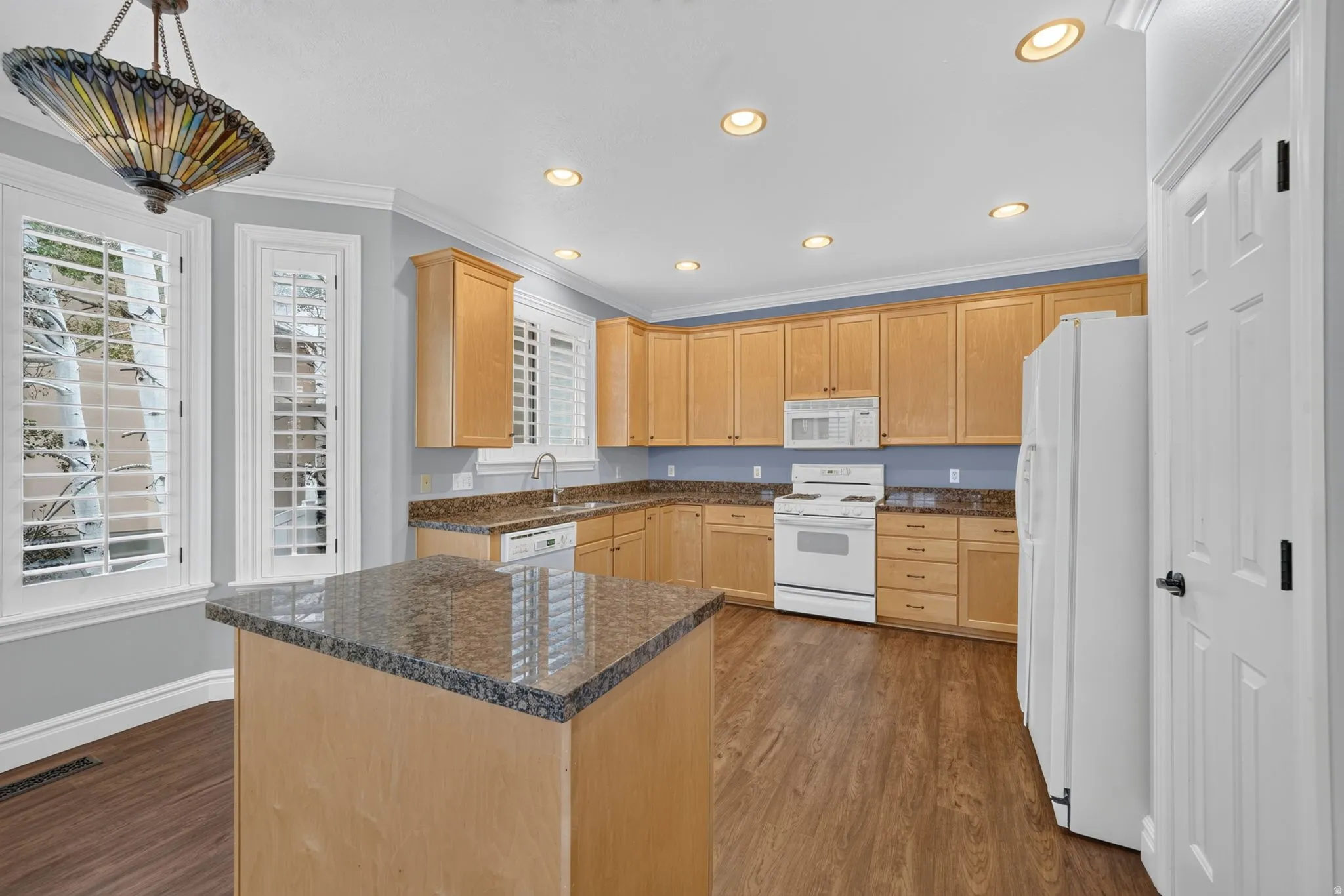 Kitchen featuring wood-finish flooring, recessed lighting, wood cabinetry, granite countertops, and white appliances