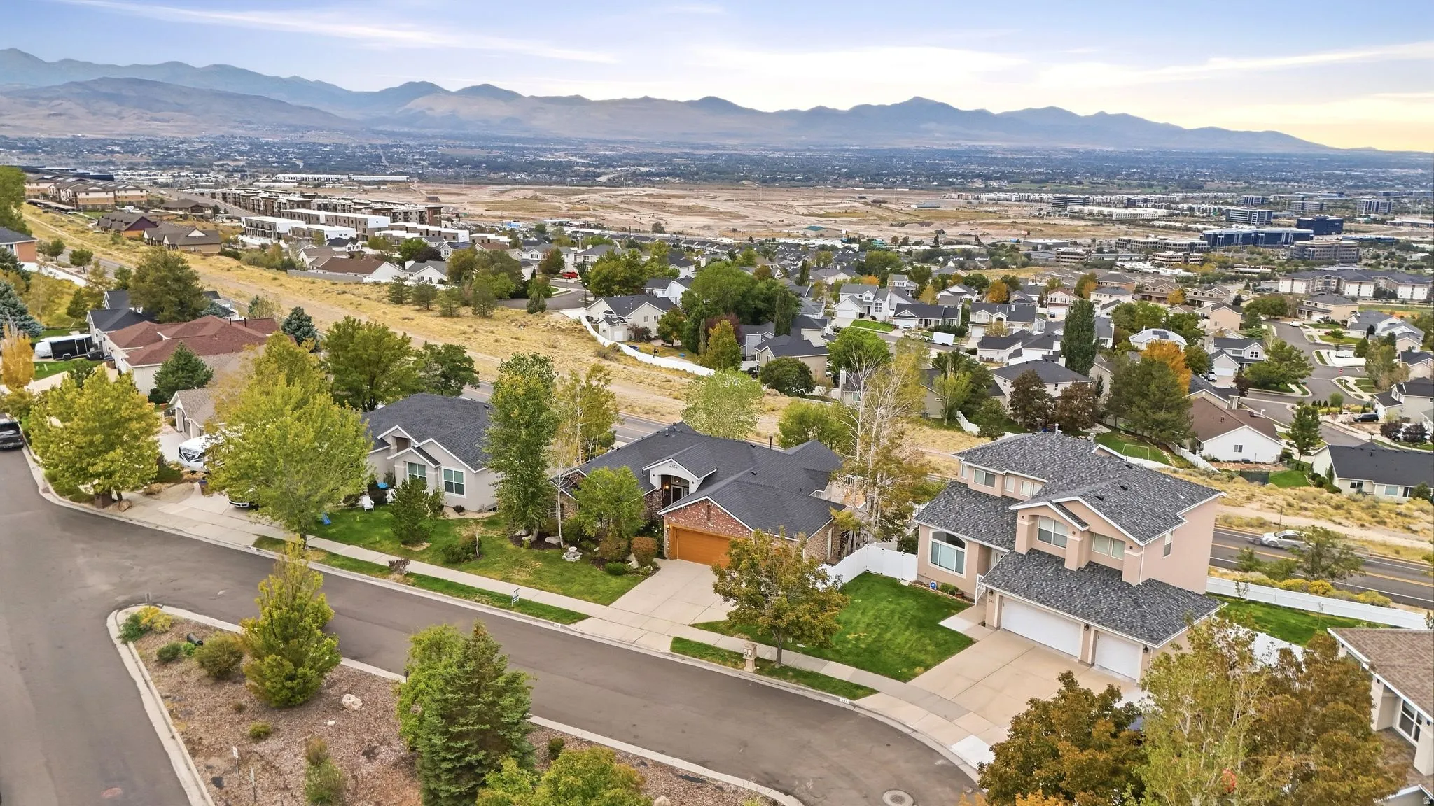 Residential neighborhood featuring a paved street, mature trees, and distant mountain scenery