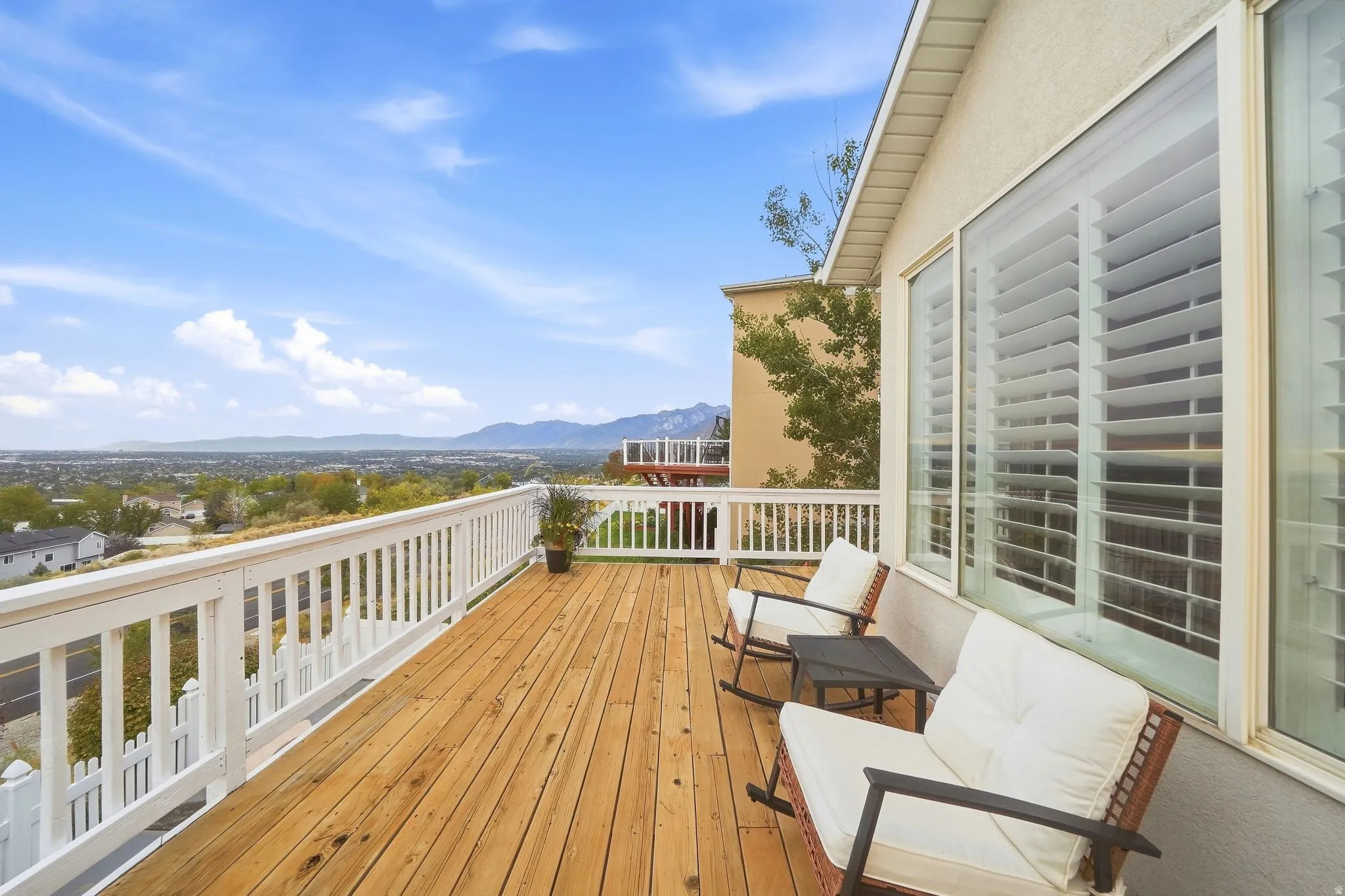 Expansive wood deck with white railing, stucco exterior, and large windows with plantation shutters