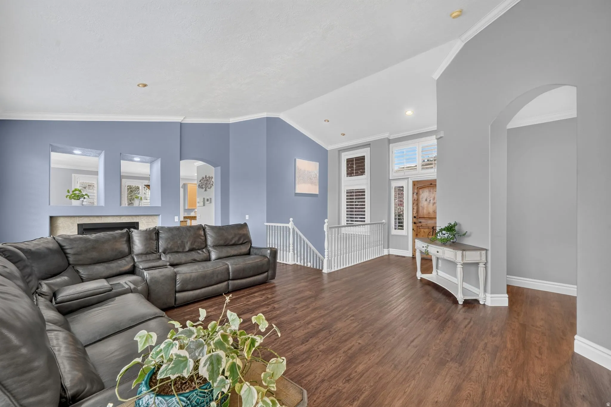 Wood-finish flooring throughout, featuring a fireplace with a light-toned surround, a staircase with white balusters, an arched doorway, and built-in wall cutouts
