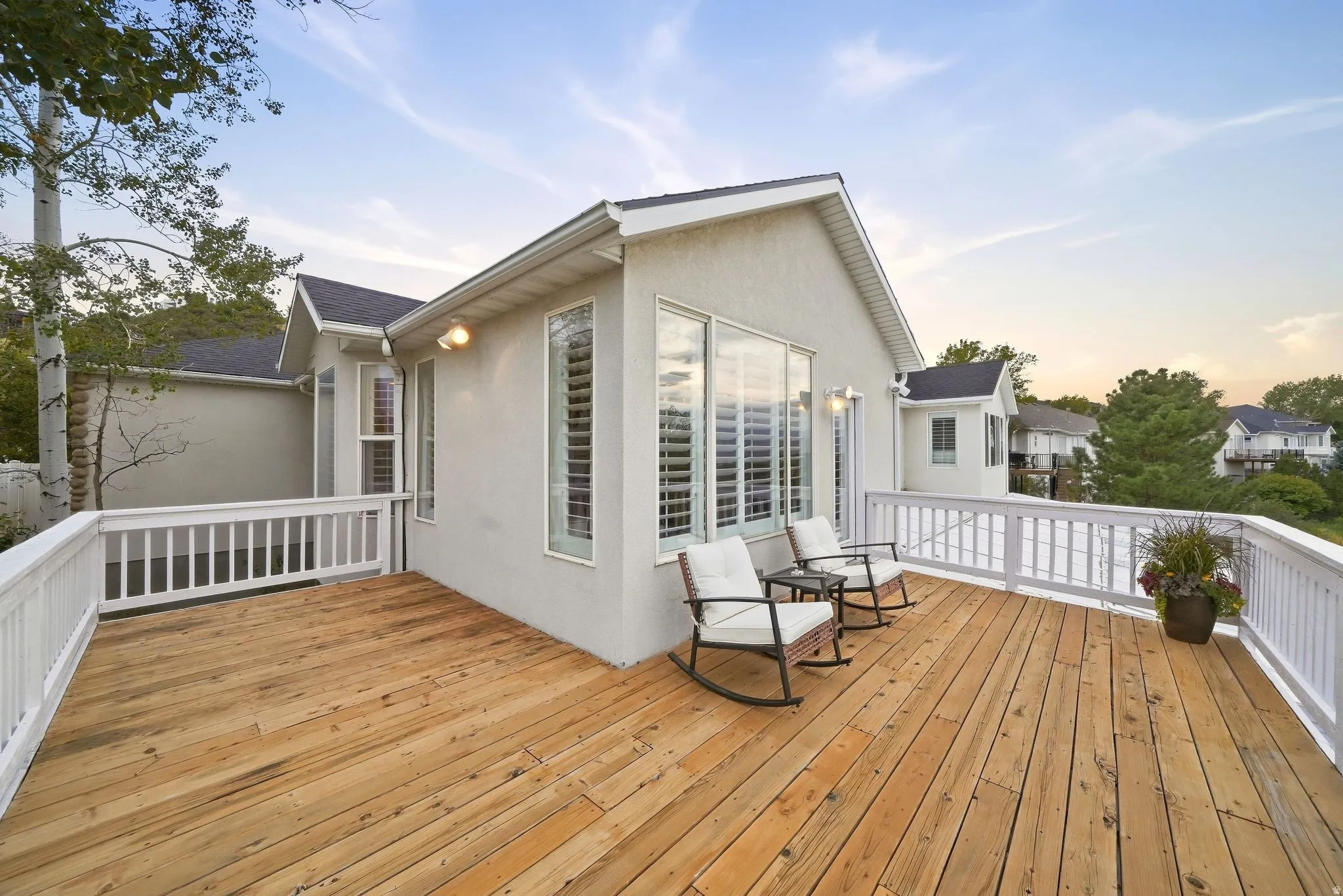Expansive wood deck with white railing, featuring a stucco exterior and multiple windows with plantation shutters