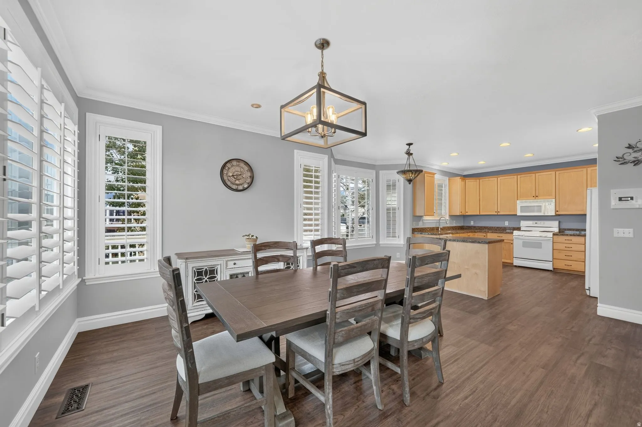 Open-concept kitchen and dining area featuring wood-finish flooring, custom window shutters, and a bay window
