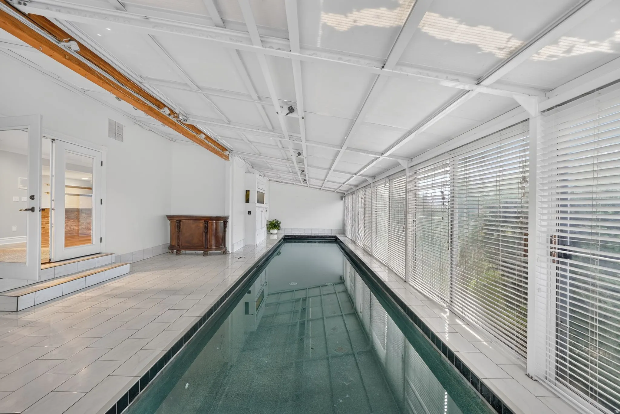 Indoor swimming pool with tile surround, white walls, and a translucent paneled ceiling
