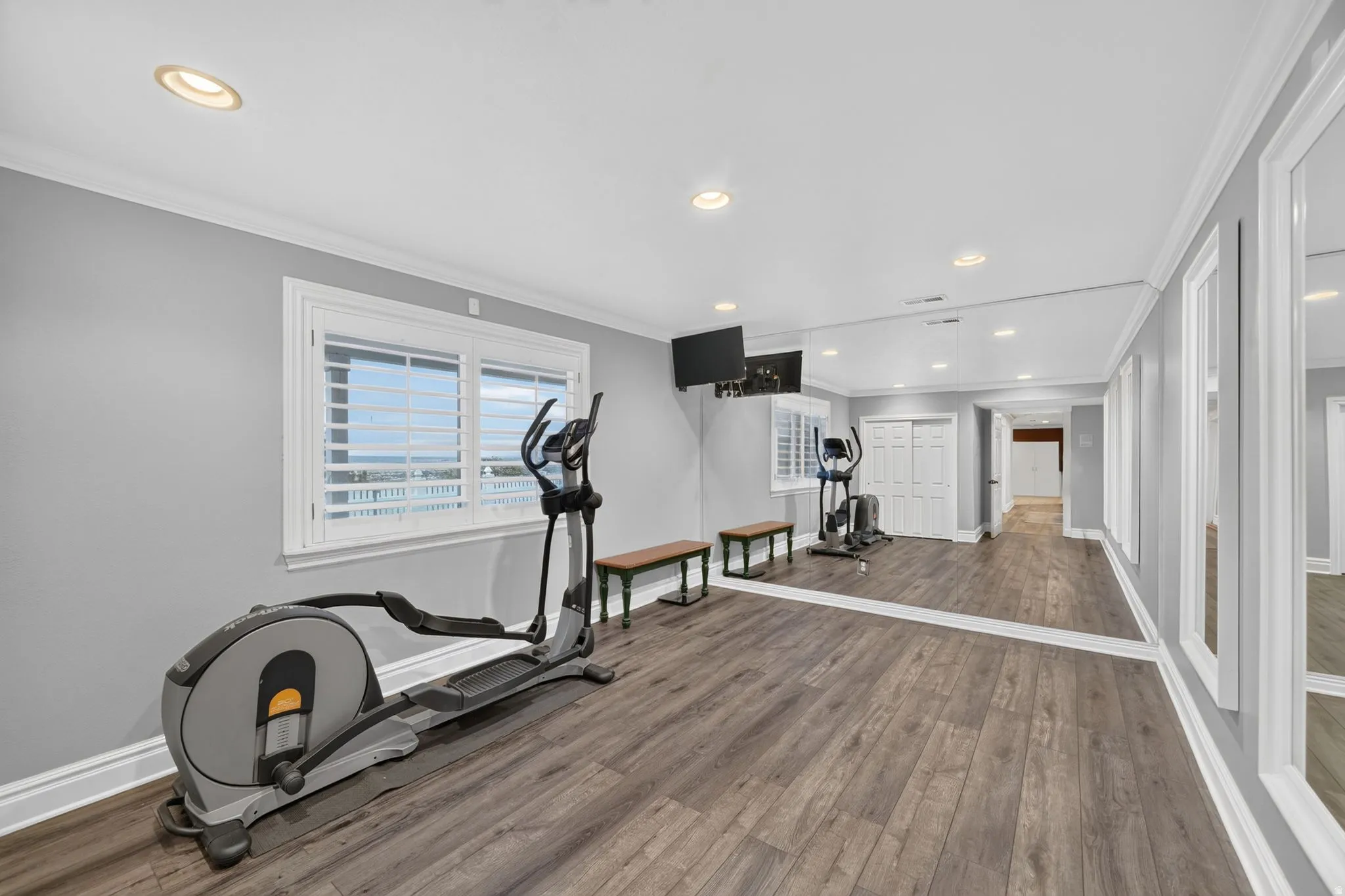Recessed lighting, wood-finish flooring, full-length wall mirrors, windows with plantation shutters, and crown molding
