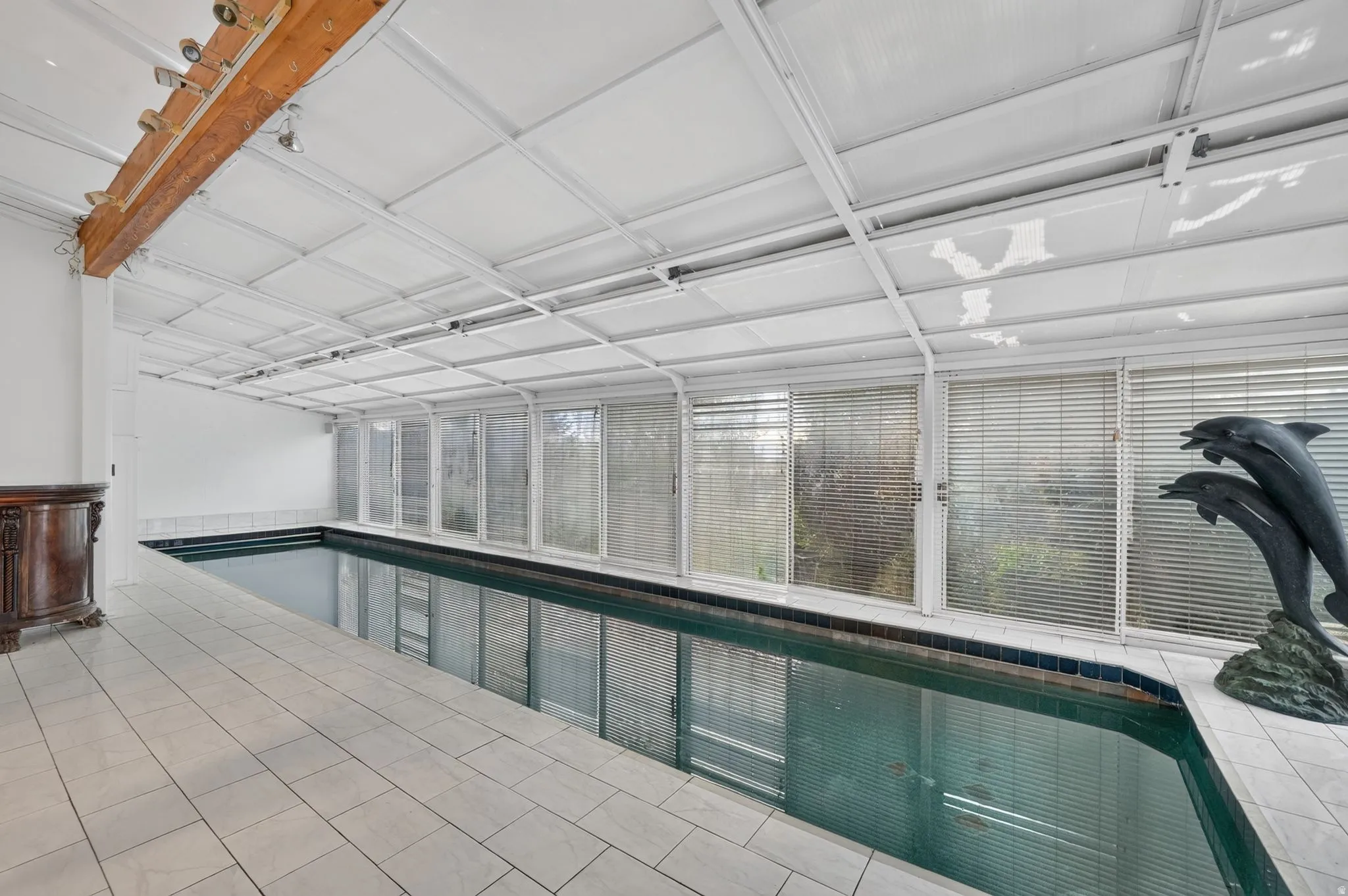 Indoor swimming pool with tile surround, full-height windows, and a structured ceiling