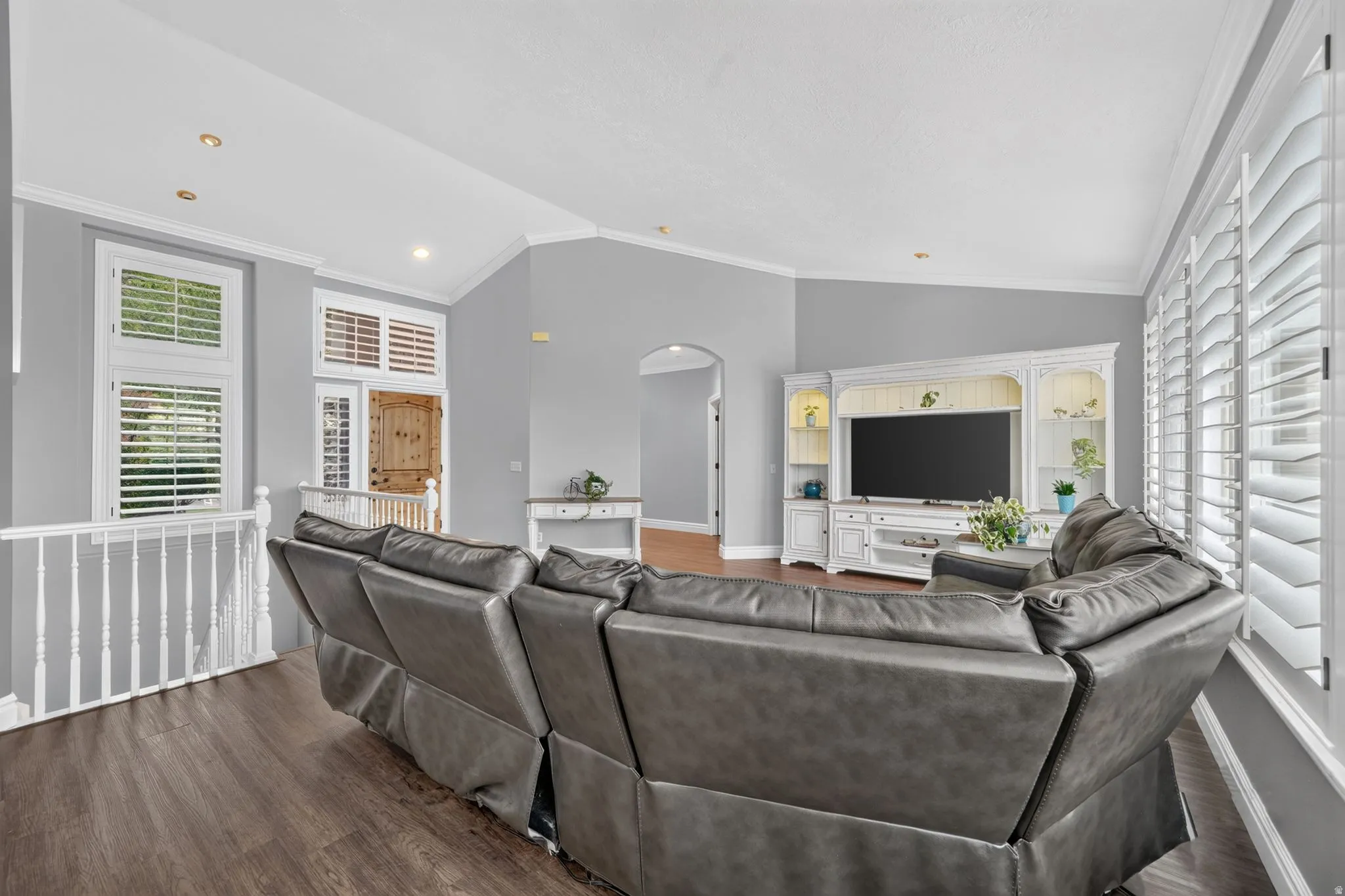 Wood-finish flooring, white plantation shutters, vaulted ceiling, recessed lighting, and a built-in media console