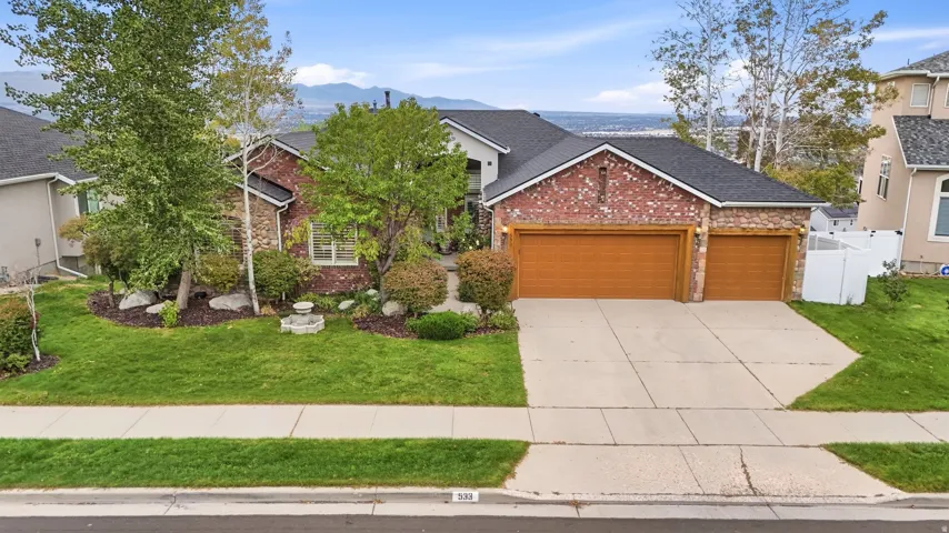 Brick and stone facade with a multi-car garage, mature landscaping, and a manicured lawn