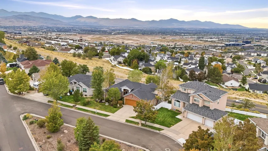 Residential neighborhood featuring a paved street, mature trees, and distant mountain scenery