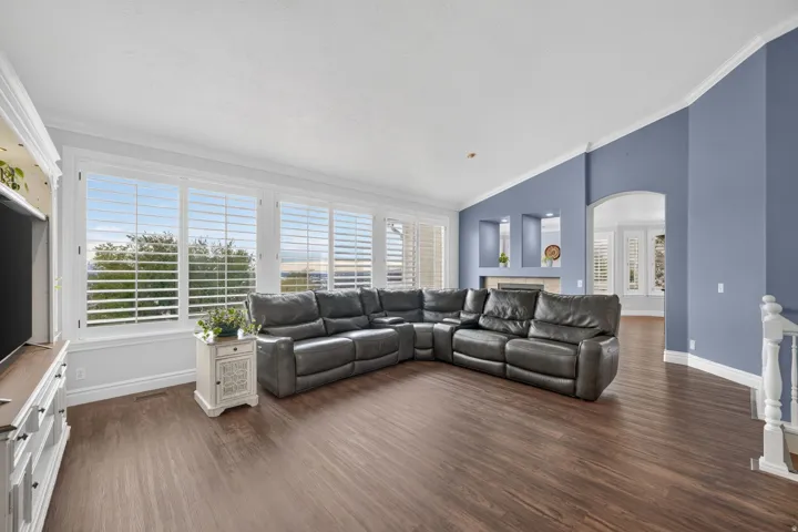 Extensive wood-finish flooring, multiple large windows with plantation shutters, vaulted ceiling, built-in shelving, and a decorative archway