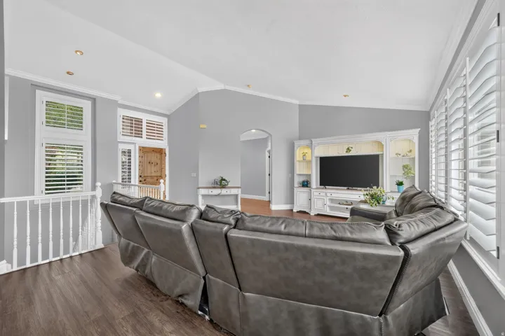 Wood-finish flooring, white plantation shutters, vaulted ceiling, recessed lighting, and a built-in media console