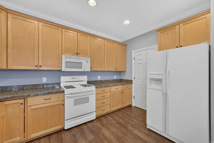 Kitchen with wood-finish cabinetry, speckled countertops, white appliances, and wood-finish flooring